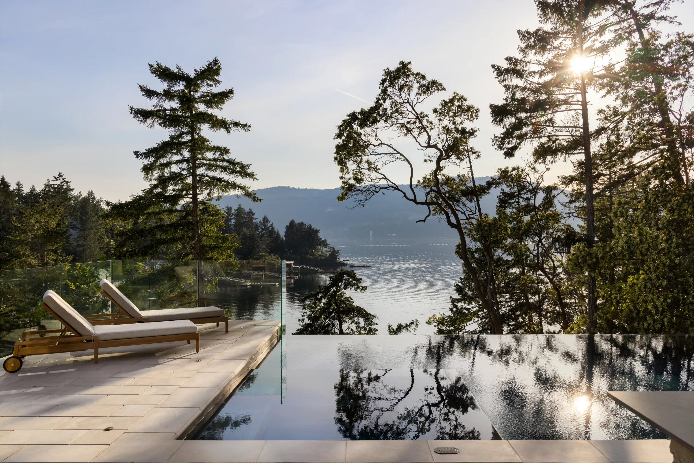 Infinity pool edged in cut stone with teak loungers, firs and arbutus framing the inlet beyond
