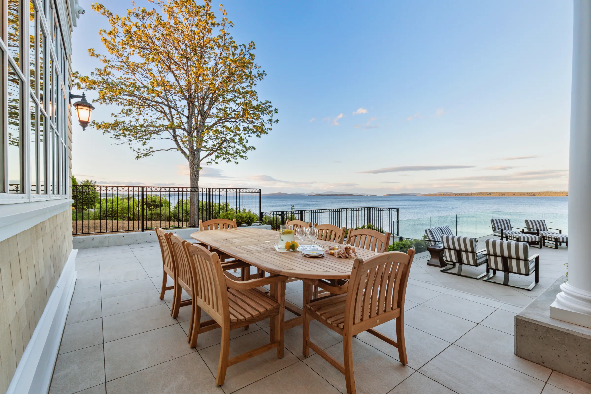 Teak dining table for eight on a stone terrace, shingled wall and iron fence above the water